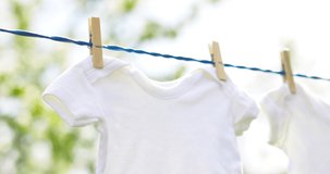 White baby clothes hanging on rope outdoors on spring day