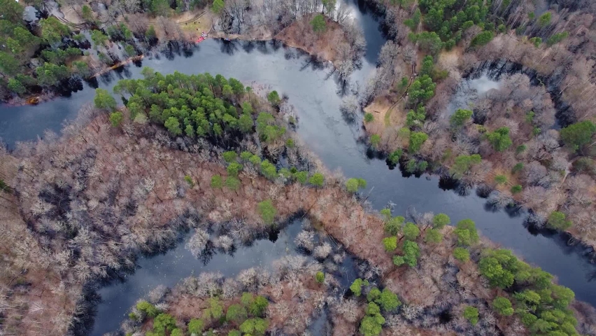 Aerial view of the river between the pines. Flying over a winding riverbed surrounded by green treetops. Epic panoramic shot. Spring flood of water. Kayaking trip