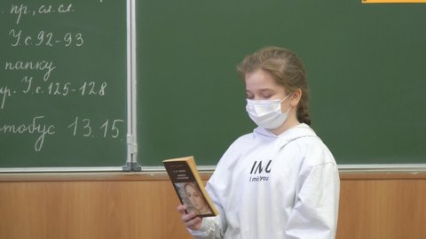 Chapaevsk, Samara region, Russia - February 21, 2022: A schoolgirl in a protective mask with a book in her hands stands at the blackboard and tells a lesson