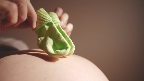 happy pregnant woman. booties baby shoes on the belly of a pregnant woman. pregnancy health procreation concept. close-up belly of a pregnant woman. woman waiting for a newborn baby indoor