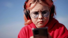 chubby child girl is playing video game in smartphone, listening to music by headphones