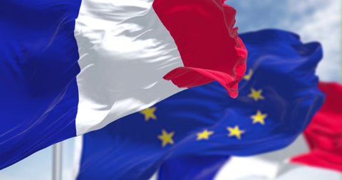 Seamless slow motion loop of the national flag of France waving in the wind with blurred european union flag in the background on a clear day. European country. Selective focus.