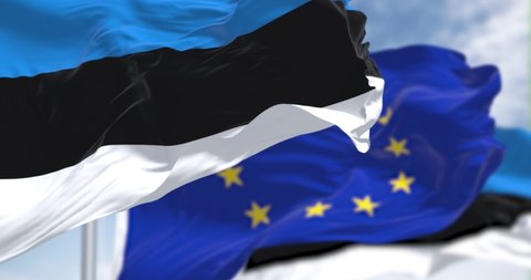 Seamless slow motion loop of the national flag of Estonia waving in the wind with blurred european union flag in the background on a clear day. European country. Selective focus.
