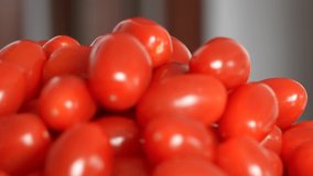 Close up view 4k stock video footage of pile of tasty fresh juicy small oblong organic tomato cherry vegetables isolated on plate in blurry kitchen interior background. Food abstract video backdrop