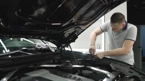 Repairman - auto mechanic, works in a car repair shop. Installation of parts under the hood. The master installs rubber bands under the hood of the car.