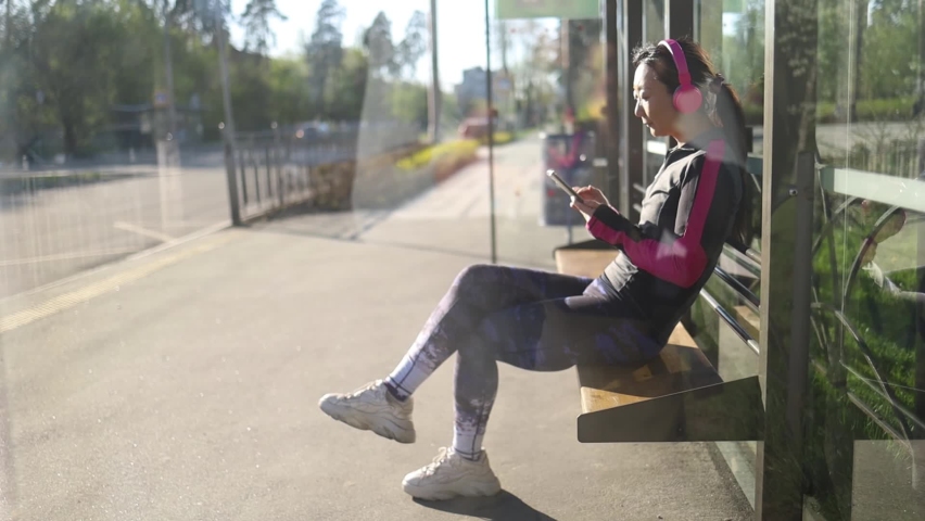 Asian woman use of mobile phone and wait for the bus at outdoor

