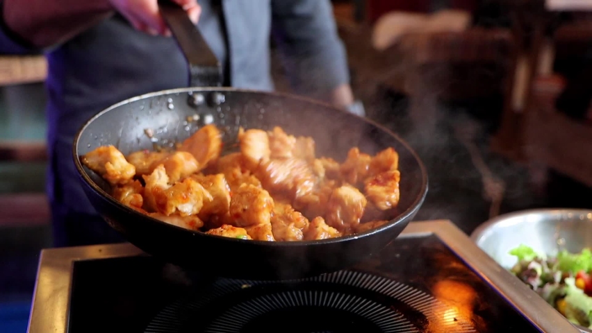 Slow motion of cook roasts chicken meat in sauce, tosses it in frying pan. Royalty-Free Stock Footage #1089951531
