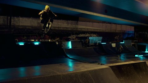 Extreme bmx biker jumping on ramp with bicycle at night outdoors. Active guy cyclist performing jump stunt on bmx bike at skate park. Healthy lifestyle active leisure enjoyment hobby concept. 