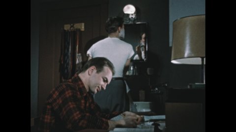 1950s: Boy sits at desk in college dorm room and speaks to friend at basin.