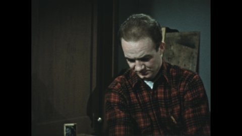 1950s: Boy walks to dresser in dorm room and speaks. Boy leans on dresser and looks at photo of girl.