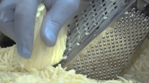 hand in a glove rubs hard cheese on a metal grater