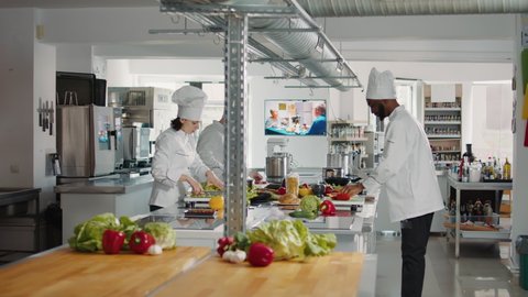 Man and woman cutting fresh ingredients to make gourmet dish, doing teamwork to prepare vegetables for gastronomic meal. Professional chefs in uniform cooking organic food in kitchen cuisine.