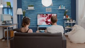 Couple disappointed because of losing online console space shooter while playing using wireless controller while sitting on couch. Young woman and boyfriend arguing over failed level in action game.