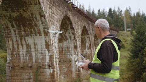Drone under a bridge doing an inspection. Drone operator next to flyover. Quadcopter for observation of bridge. Road and bridge maintenance technologies. Engineer man with drone. Aerial monitoring.
