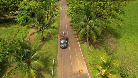 AERIAL TOP DOWN: SUV car with livestock trailer avoiding potholes on tropic road. Winding vehicle bypassing asphalt holes in exotic countryside. Damaged infrastructure in third world.