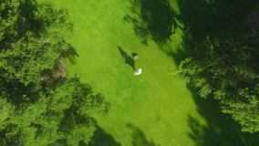 4K aerial footage energetic woman in white dress looking up in drone camera and taking off white hat on summer day. Happy young cheerful girl spinning around outdoors on green lawn Video series 1 of 6