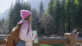 Smiling woman drinks water from hiking bottle, relaxing on nature adventure in Yosemite Valley, autumn spring sunny day. Health care, authenticity, sense of balance and calmness. RED camera 6K Video