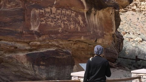 A woman looks at ancient petroglyphs on a rock wall at Nine Mile Canyon in Utah.