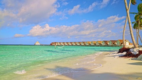 Tropical Maldives island atoll with picturesque palm tree lined sandy beach and turquoise clear water with overwater bungalows