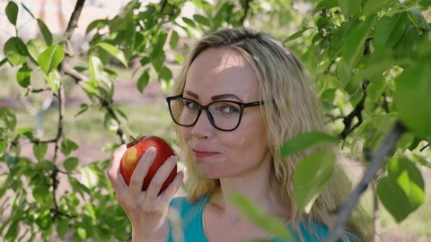 portrait of a young woman biting and eating a ripe red apple, looking at the camera in the garden, slow motion. Healthy food and beauty. diet