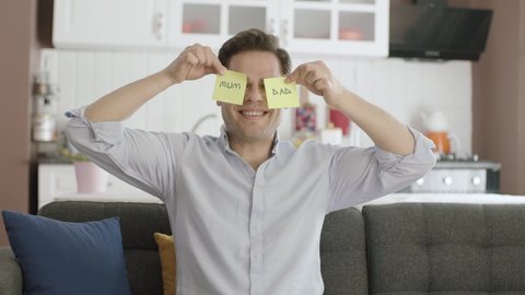 Video of happy man dancing holding paper notes with mom and dad over his eyes.Man dancing on the sofa of his house with papers in his eyes.Valentine's day, mother's day, father's day,romantic concept.