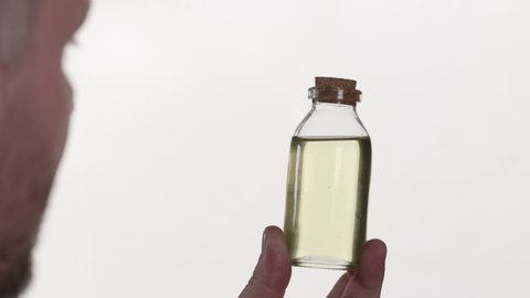 Over-shoulder shot of a man holding a small glass jar in his hand. There is a yellow liquid in the vessel. Close look to the liquid.
