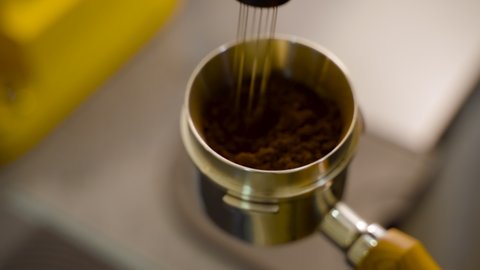 close up of a man distributing ground coffee in a portafilter using distributor needle