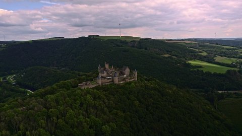 Aerial footage Cinematic B-Roll: Drone at Bourscheid Castle. On top of the mountain the beautiful castle and in the valley a view of a river, meadows, hills, forests and a windmill. Luxembourg.