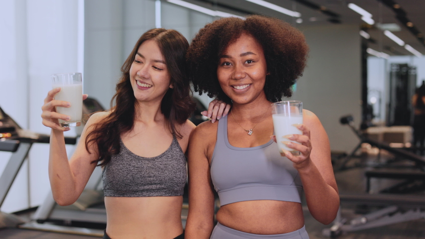 Young Asian and African American woman finishing workout and drinking protein milk shake vitamins after training. Bodybuilding. Healthy Friend lifestyle. Royalty-Free Stock Footage #1089971419