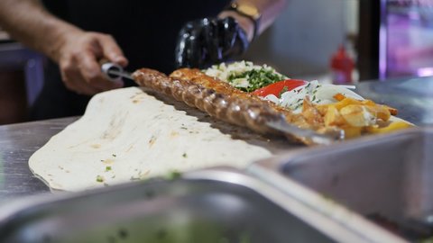 a restaurant shish kebab removes a kebab from a skewer on a thin pita bread with vegetables and fragrant greens cut into pieces. National Armenian food