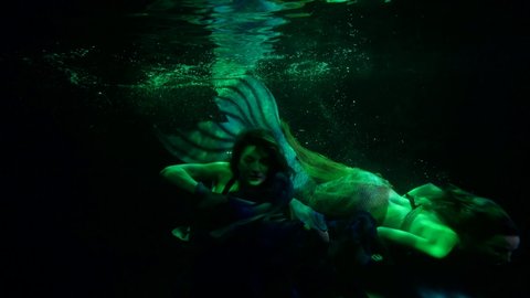 two mermaids are swimming in mysterious dark of ocean depth, slow motion enigmatic shot