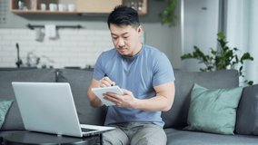 Young asian male studying for university at home via online lessons. Distance education. man using laptop for e-learning remotely learning Asks for advice on a video call consult, writes in a notebook
