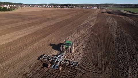 John Deere Tractor with cultivator plowing field. Tractor disk harrow on ploughing a soil. Planting in farmland. Sowing seed on plowed field. Farm Machinery cultivating. Russia, Smolensk, 04.26.2022.