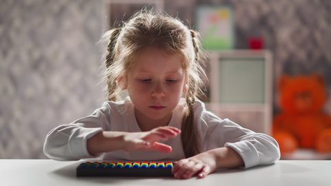 Serious little schoolgirl with blonde thin braids learns to do sums with abacus at home mental arithmetic lesson close view slow motion