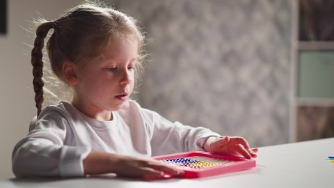 Thoughtful little girl student plays with colorful plastic abacus sitting at table during mental maths lesson in children room closeup slow motion