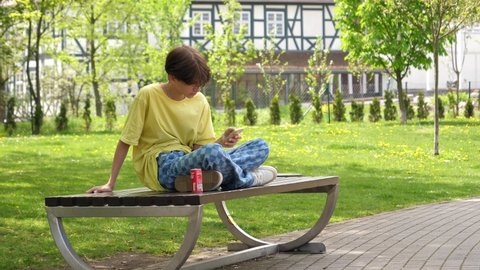 WROCLAW, POLAND - MAY 06, 2022: Teenager kid boy sit on a bench in park watch use smart phone device alone