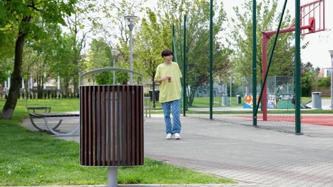 WROCLAW, POLAND - MAY 06, 2022: Drink up and throw out coca cola red can in a trash bin on a park alley by teenager kid boy