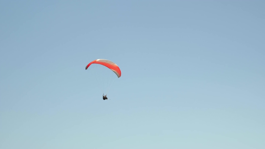 Red parachute flying against clear blue sky. Paragliding extreme sports. Person paragliding over sea coastline in sky. Adrenaline and extreme sport. Recreation activity. Travel and tourism concept