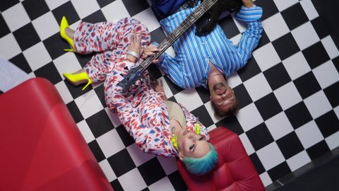 a couple, a man playing the electric guitar and a travesty actor lie on the floor with a checkerboard pattern. rotating image.