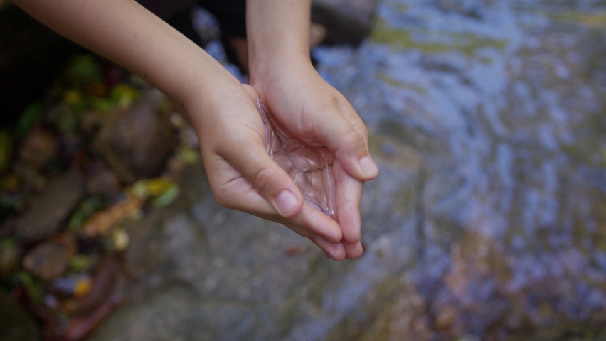 The child collects water from the river in his hands, holds it, and then pours it out. The concept of environmental protection, water pollution and microplastics. | Shutterstock HD Video #1089981703