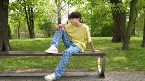 WROCLAW, POLAND - MAY 06, 2022: Teenager boy kid drinks cola beverage from a red can sitting on a park bench in a city