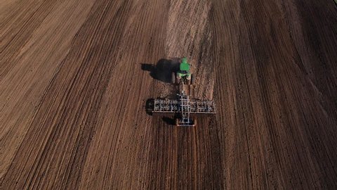 John Deere Tractor with cultivator plowing field. Tractor disk harrow on ploughing a soil. Planting in farmland. Sowing seed on plowed field. Farm Machinery cultivating. Russia, Smolensk, 04.26.2022.