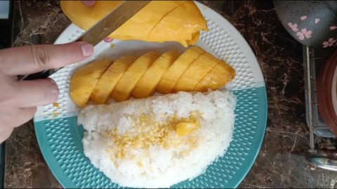 Girl peeling mango and hold it in hand, cutting by knife. peeling ripe mango, ripe mango and the paring Thai Sweet Sticky Rice with Mango (Thai Dessert) or Khao Niew Ma Muang top view.