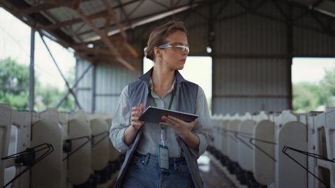 Livestock worker walking animal husbandry. Professional breeder holding tablet. Focused woman farming engineer checking feedlots inspecting empty shed at countryside. Agricultural specialist concept