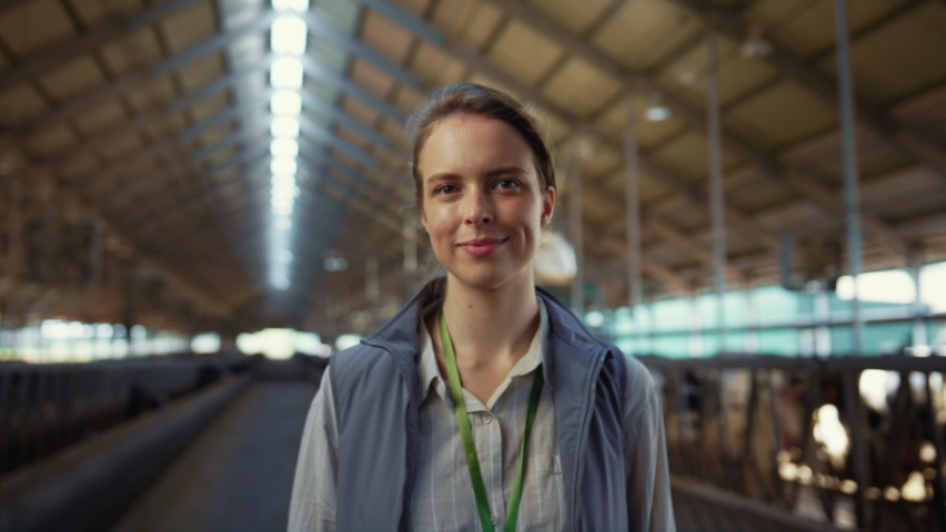 Smiling woman posing shed aisle alone portrait. Agricultural specialist at work. Beautiful smiling woman farm veterinarian looking in camera at cowshed feedlots. Professional agribusiness manager. Royalty-Free Stock Footage #1089986205