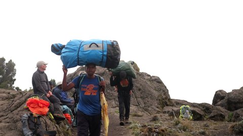 Kilimanjaro. Tanzania. Africa - 12.25.2021 Tourists rest on the trail on the way to the Shira camp, porters with large trunks pass them while climbing Mount Kilimanjaro