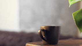 Steam rises over a black coffee cup on a wooden table against the backdrop of a sofa in a cafe. Capture 4K video in real time. Morning coffee in a cafe, break for breakfast
