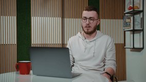 A man with glasses in front of a laptop takes off his glasses and wipes his eyes