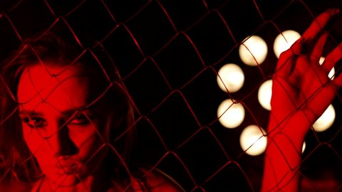 voluptuous woman is stroking metal grid and posing seductively in dark red light