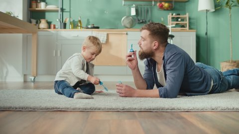 A Cheerful Father With Adorable Son Spent Time Together at Home. A Best Dad Blow Bubbles For Her Kid Son. Amazing Family Day in the Kitchen. Home Office and Parenthood at the Same Time.